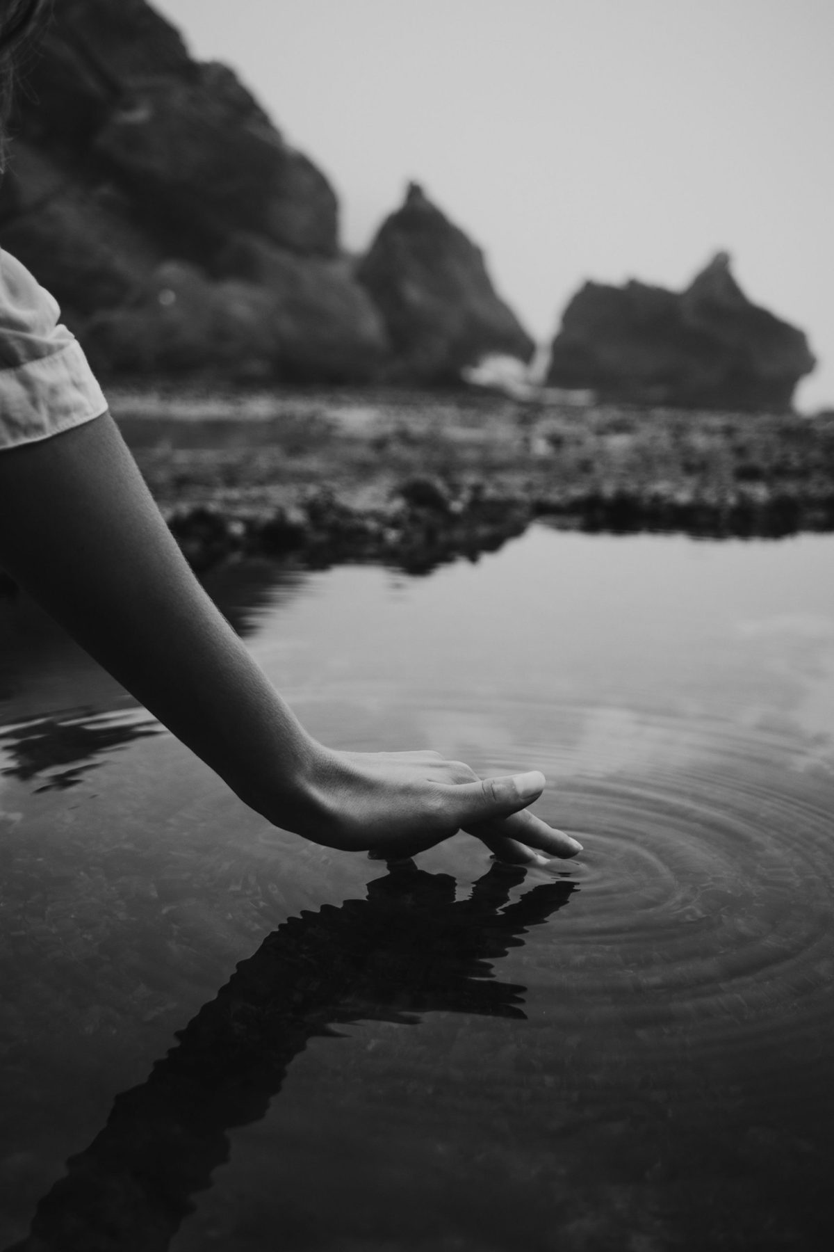 A hand touches still water, sending out rings of ripples